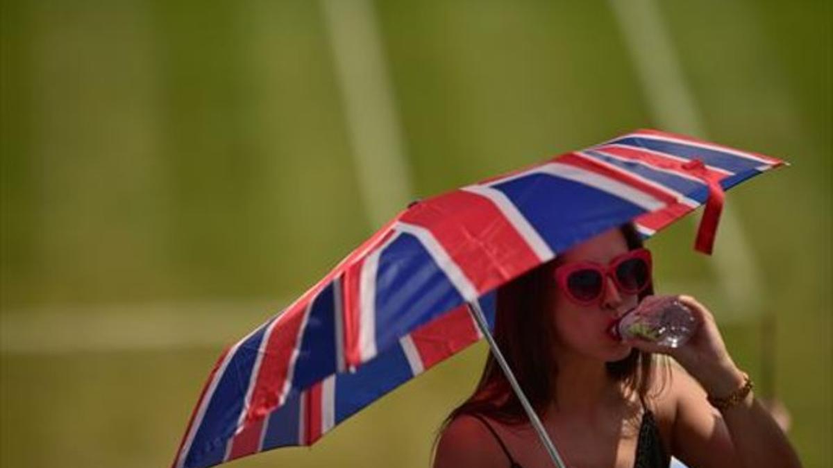 Una aficionada se protege del sol con un paraguas, en Wimbledon.