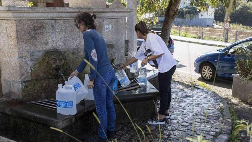 Dos vecinas recogen agua en una de las fuentes públicas de la parroquia de Bembrive. // Cristina Graña