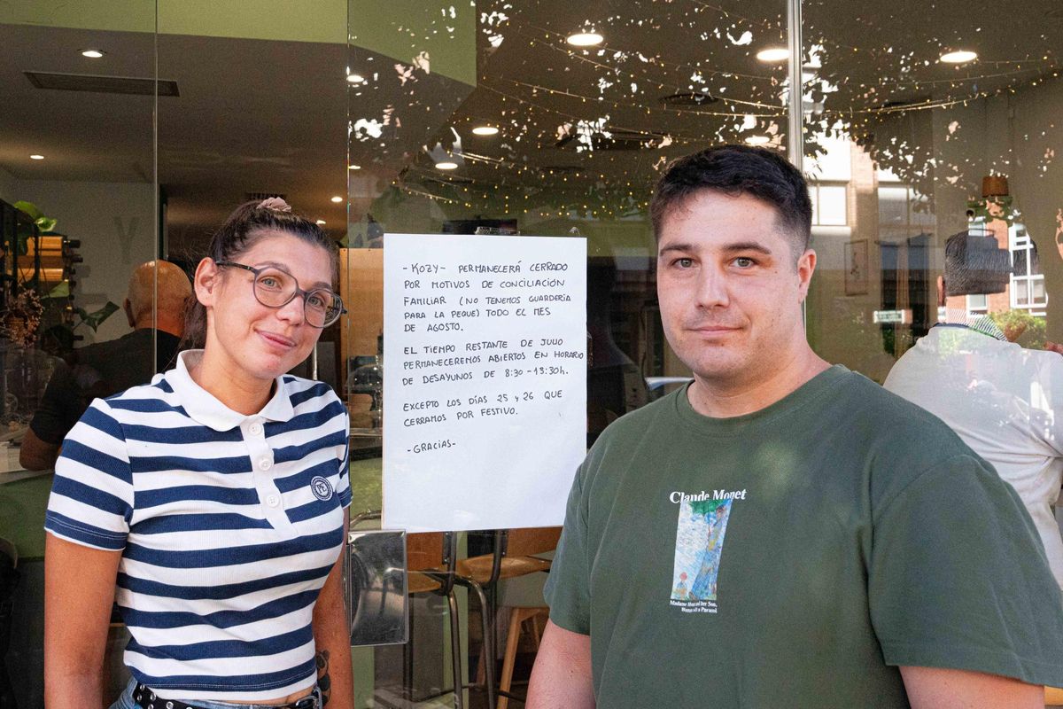 Los dueños de la cafetería Kozy, con un cartel en su puerta en el que explican que cierran en agosto por no poder conciliar (historia en el interior).