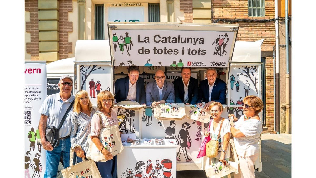 El conseller Moreno, el delegat del Govern, el director dels ST de Drets Socials i Inclusió i l'alcalde de Sant Joan de les Abadesses amb veïns i veïnes del municipi durant la parada del vehicle informatiu.
