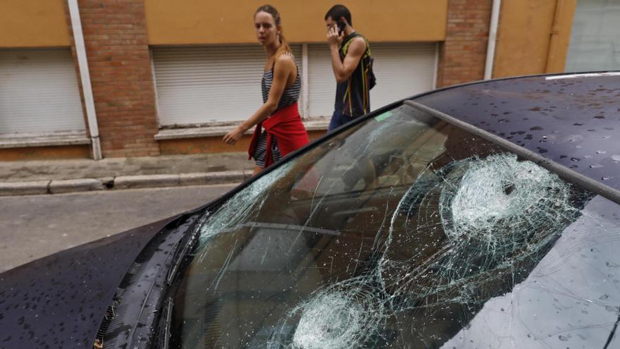 Persones passen per davant d&#039;un vehicle amb el vidre destrossat per la pedregada a la Bisbal de l&#039;Empordà | ANIOL RESCLOSA