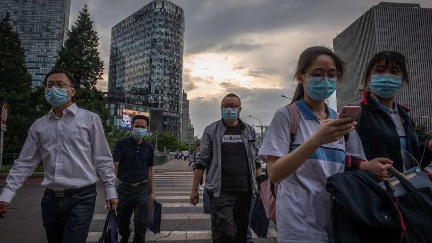 Cinco habitantes de Pekín cruzan un paso de peatones portando mascarillas quirúrgicas.