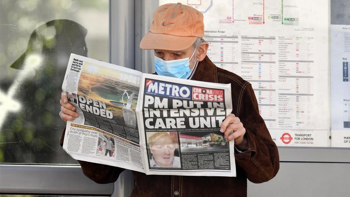 Un hombre protegido con una mascarilla lee un diario donde se informa del ingreso hospitalario de Boris Johnson por coronavirus.
