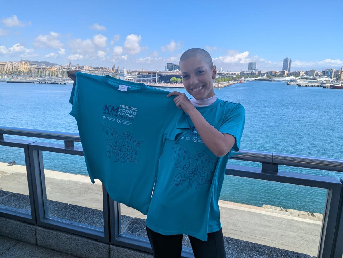 Sara Martínez muestra la camiseta de la Cursa Contra el Càncer que tendrá lugar el 31 de mayo en el Port de Barcelona.
