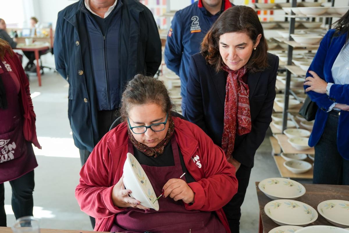 La consejera observa cómo una mujer pinta una pieza de cerámica.