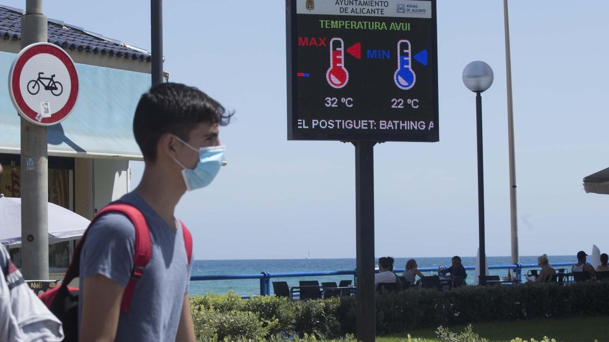 Un joven pasa junto a un termómetro en la playa del Postiguet de Alicante