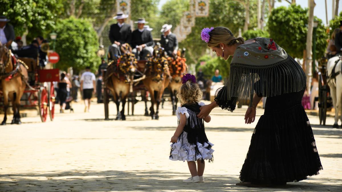 Mujer con un vestido de sevillana que agarra de la mano a una niña pequeña con un traje similar