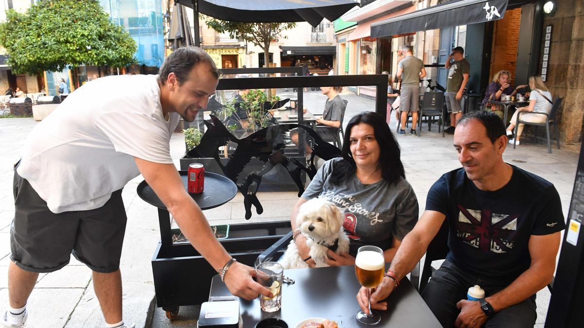 Un camarero sirve bebidas en la terraza del local Valentín a una pareja con su perro.
