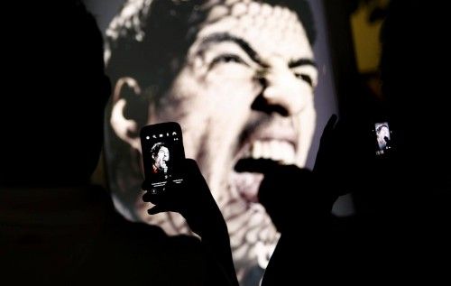 People use their mobile devices to take pictures of an advertising placard showing Uruguay's striker Luis Suarez flashing his teeth at Copacabana beach in Rio de Janeiro