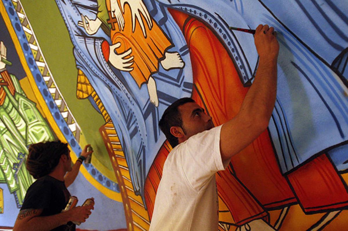Rudi (esquerra), un artista urbà expert en murals de grafits, i el seu amic House (dreta) pinten l’absis de l’església de Santa Eulàlia de Provençana, a l’Hospitalet de Llobregat, per encàrrec del rector del temple.