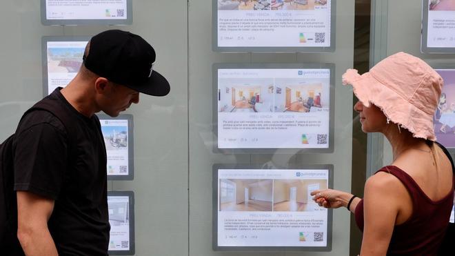Dos jóvenes miran pisos de venta y alquiler en una inmobiliaria de Barcelona.