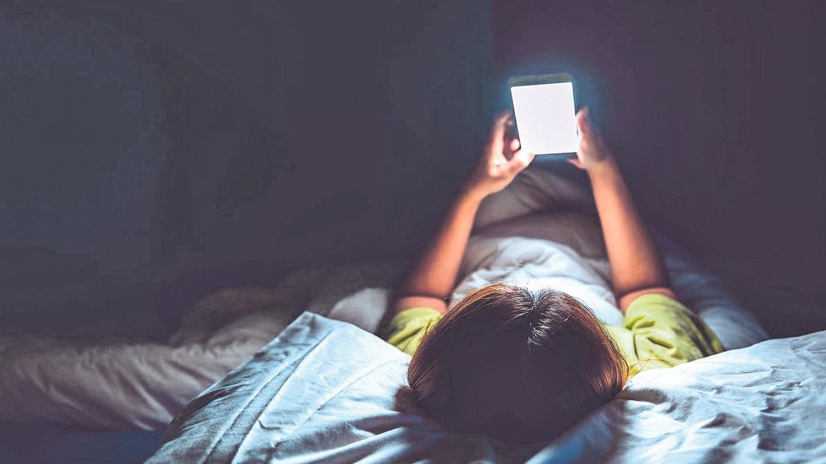 Imagen de archvio de un joven mirando el móvil antes de ponerlo a cargar junto a la cama.