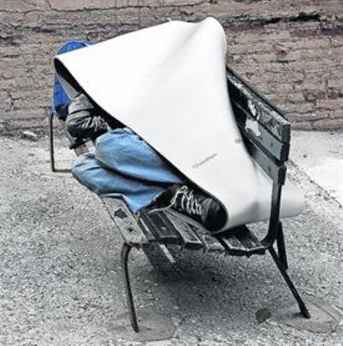 Un indigente, estirado en un banco del barrio de Gràcia de Barcelona.