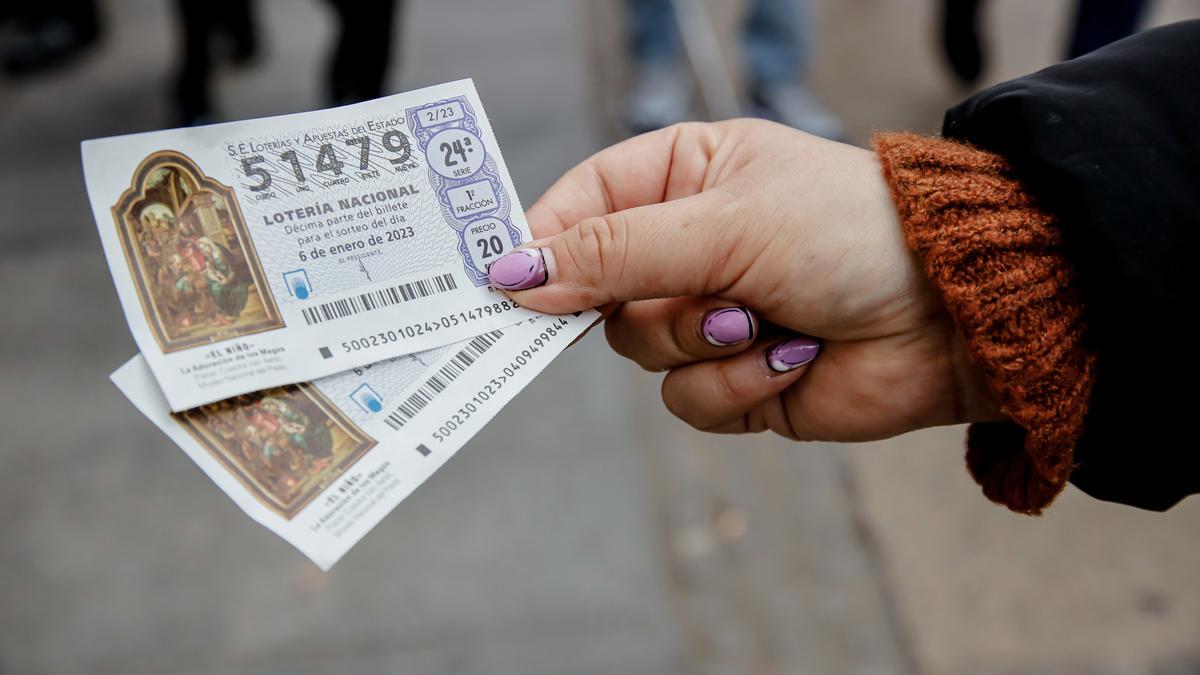 Una mujer sostiene dos décimos para el Sorteo Extraordinario del Niño.