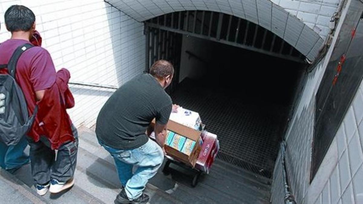 Un hombre cargado con cajas desciende penosamente por las escaleras del metro de Arc de Triomf.