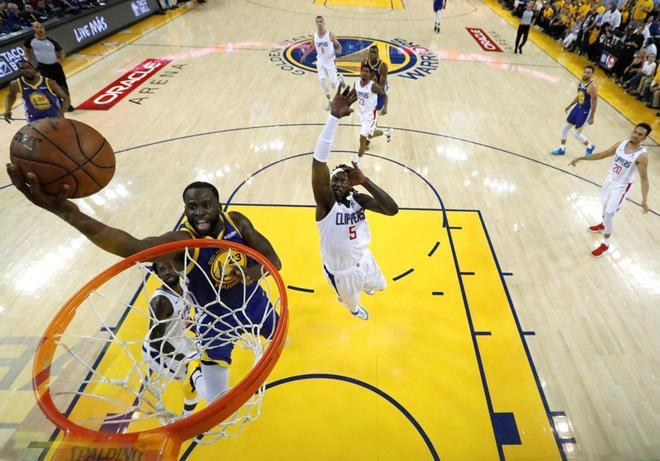 Draymond Green (2-izq) entra a canasta ante la defensa de Montrezl Harrell, durante el quinto partido de las series clasificatorias de la Conferencia Oeste de la NBA, en el pabellón Oracle Arena de Oakland, California (Estados Unidos).