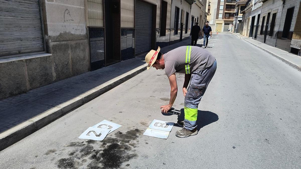 Un trabajador pinta el número de los puestos del mercadillo.