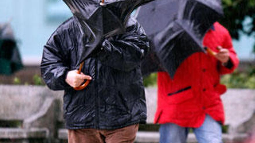 Un vecino de Bayona intenta plegar su paraguas doblado por el temporal de lluvia