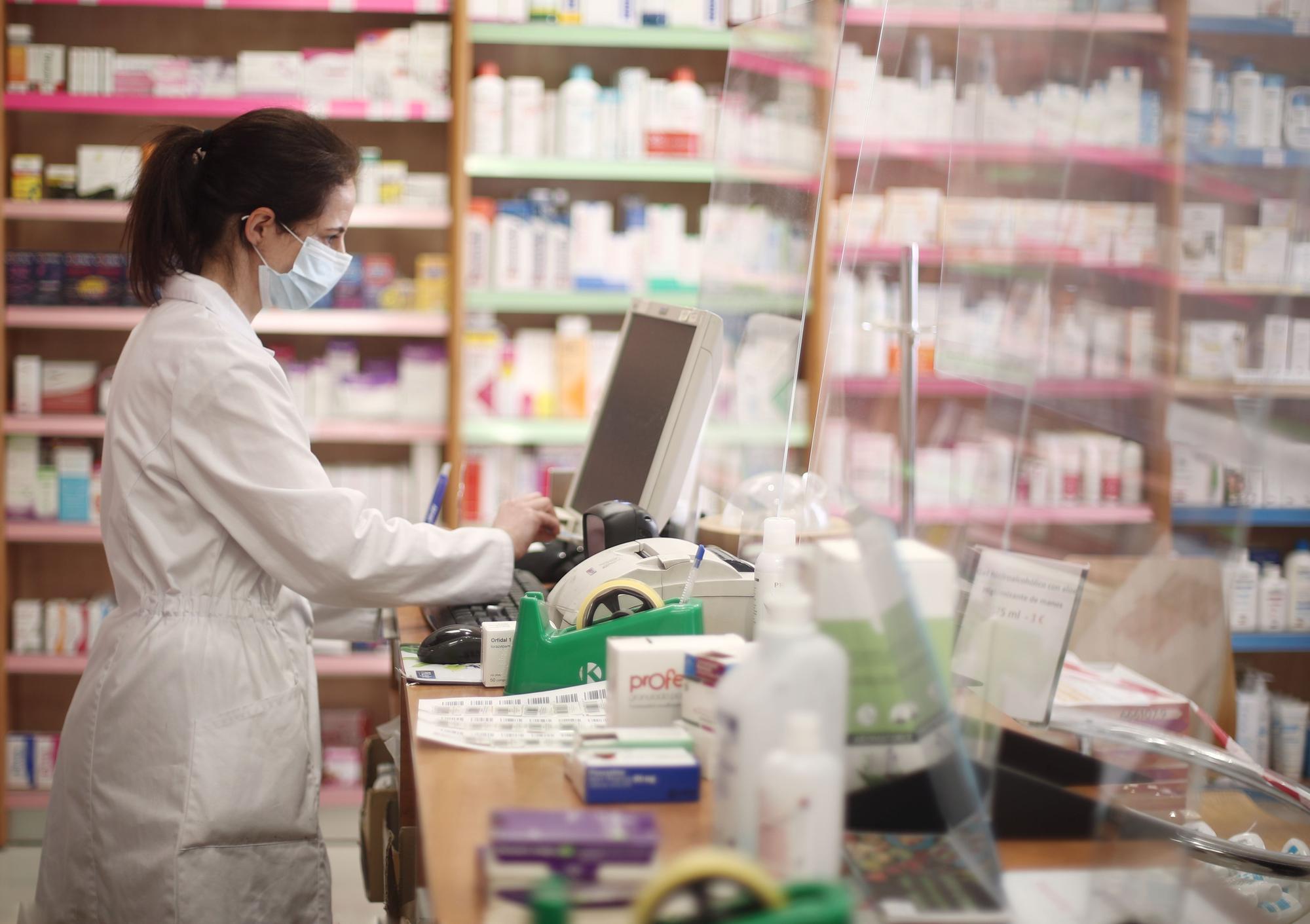 Una farmacéutica con mascarilla despacha en una farmacia.