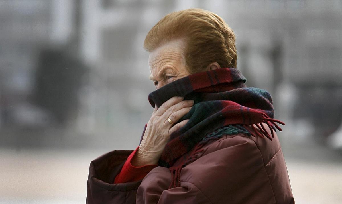 Una mujer se proteje del frío y el viento en el paseo marítimo de A Coruña