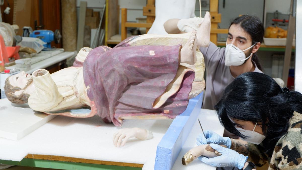 Dos estudiantes de la Escuela de Restauración trabaja sobre los pies de una talla.