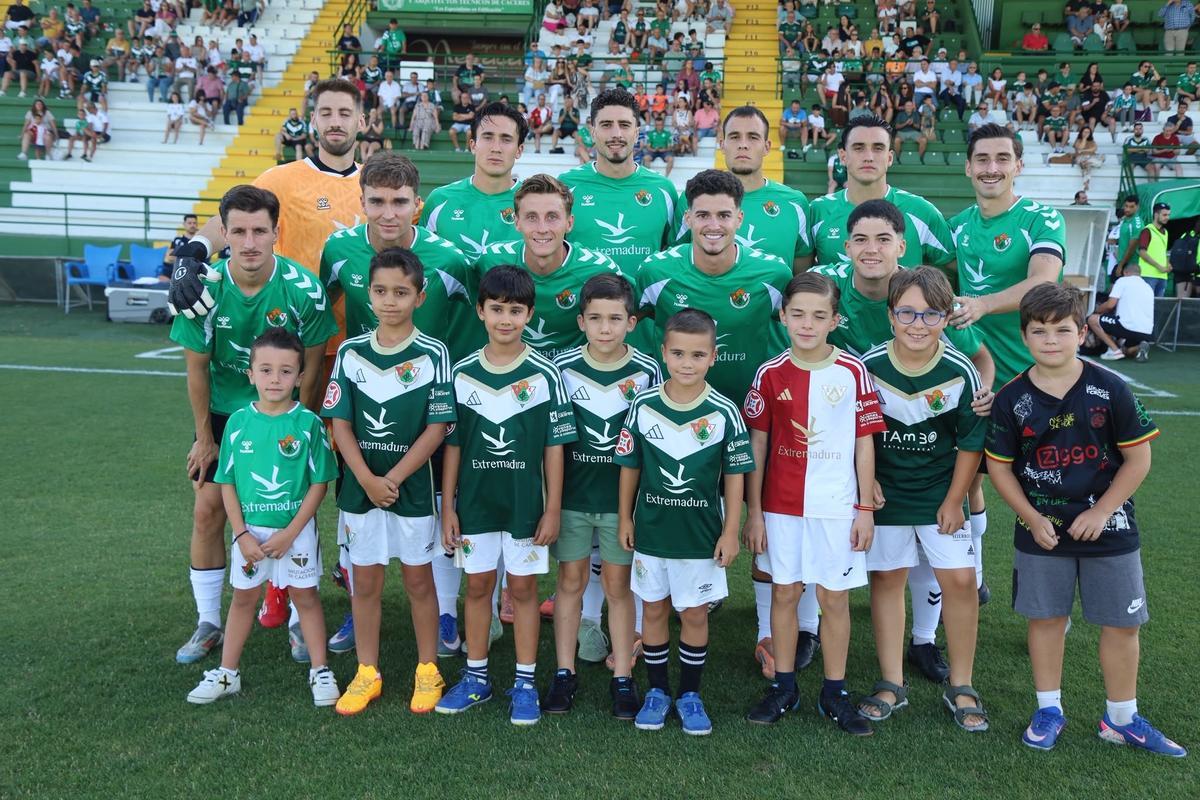 El once inicial del Cacereño, fotografiado con varios niños.