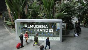 Varias personas caminan frente a la placa de la nueva denominación de la estación Madrid Puerta de Atocha Almudena Grandes.