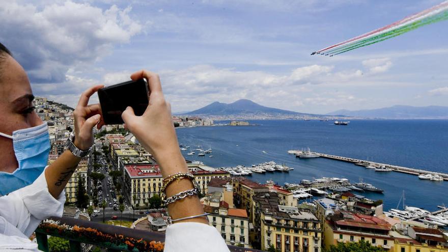 Una mujer con una máscara facial protectora usa un teléfono móvil para tomar fotos del equipo de demostración acrobática &quot;Frecce Tricolori&quot; de la Fuerza Aérea Italiana.