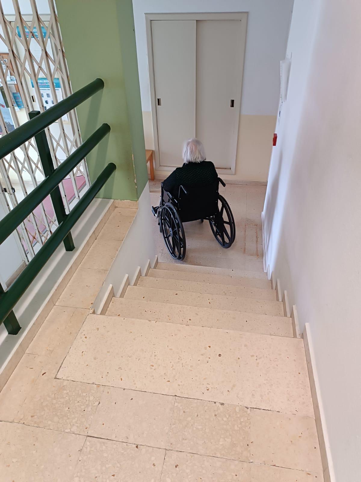 Unha muller en cadeira de rodas xunto ás escaleiras de entrada ao centro médico de Corrubedo.