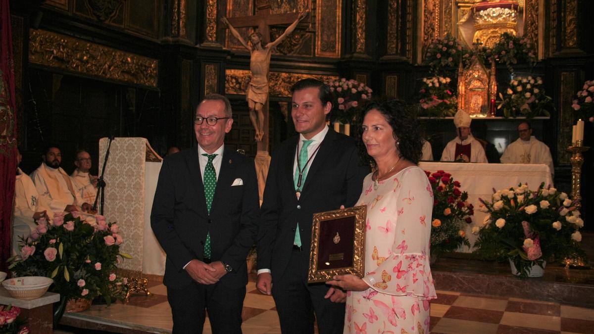 Ignacio Arcas (c) entregó al presidente del Paso Blanco, Ramón Mateos, y la vicepresidenta primera del Coro de Damas de la Virgen de la Amargura, Pilar María Salinas Pelegrín, la Medalla de Oro de la Patrona a la Santísima Virgen de la Amargura.