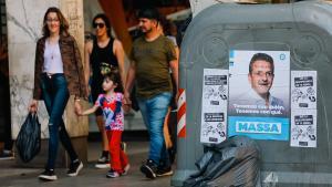 Personas caminan por una calle en Buenos Aires junto a un cartel electoral de Sergio Massa.