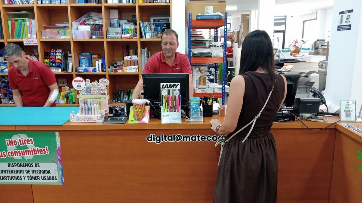 El gerente de Mateco atiende a una mujer. A la izquierda, un trabajador en la tienda de Gandia.