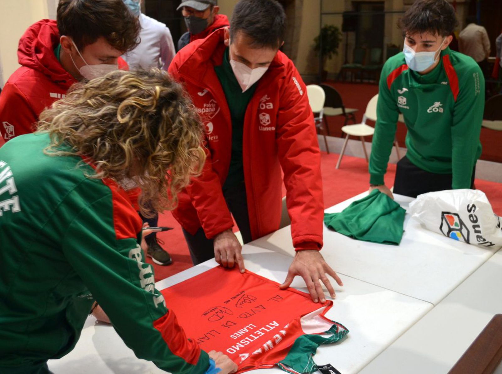 Los deportistas, firmando las camisetas.