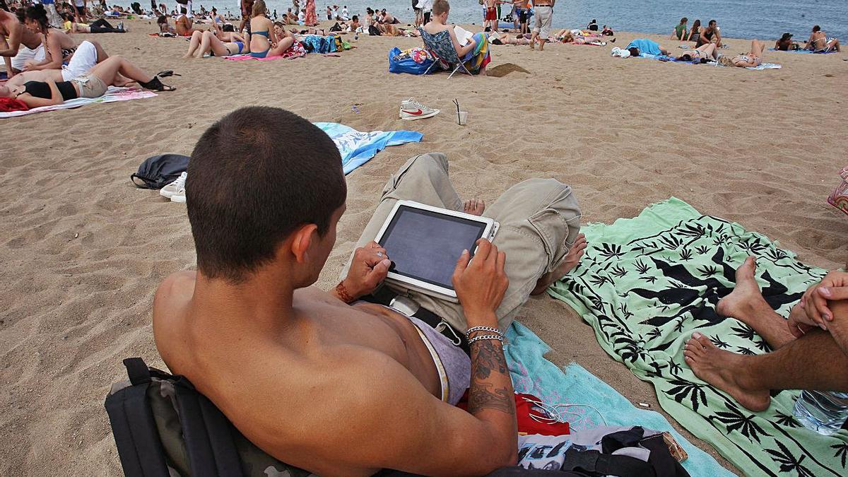 Un jove consulta el seu Ipad mentre està en una platja a Barcelona. | ELISENDA PONS