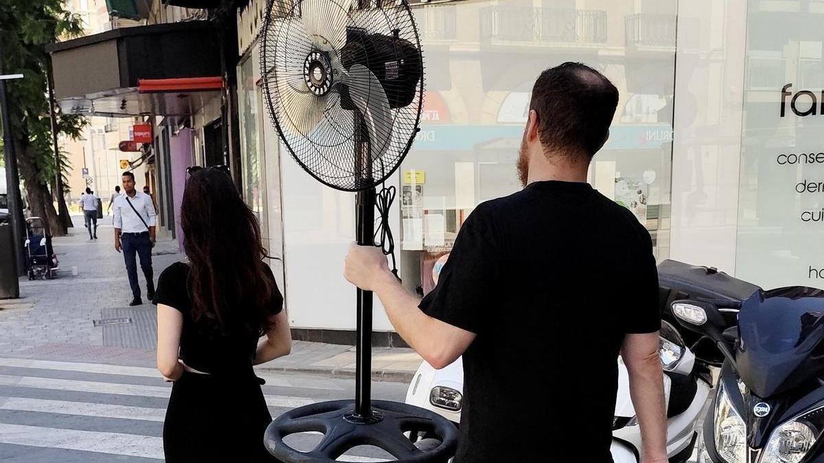 Un hombre camina por Murcia con un ventilador en la mano en un caluroso día de verano.
