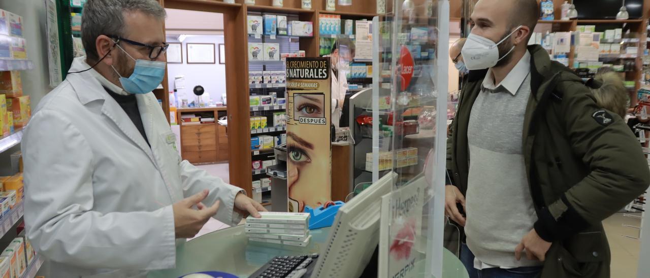 El farmacéutico Francisco Delgado explica a un cliente cómo usar los tests rápidos de coronavirus en casa.