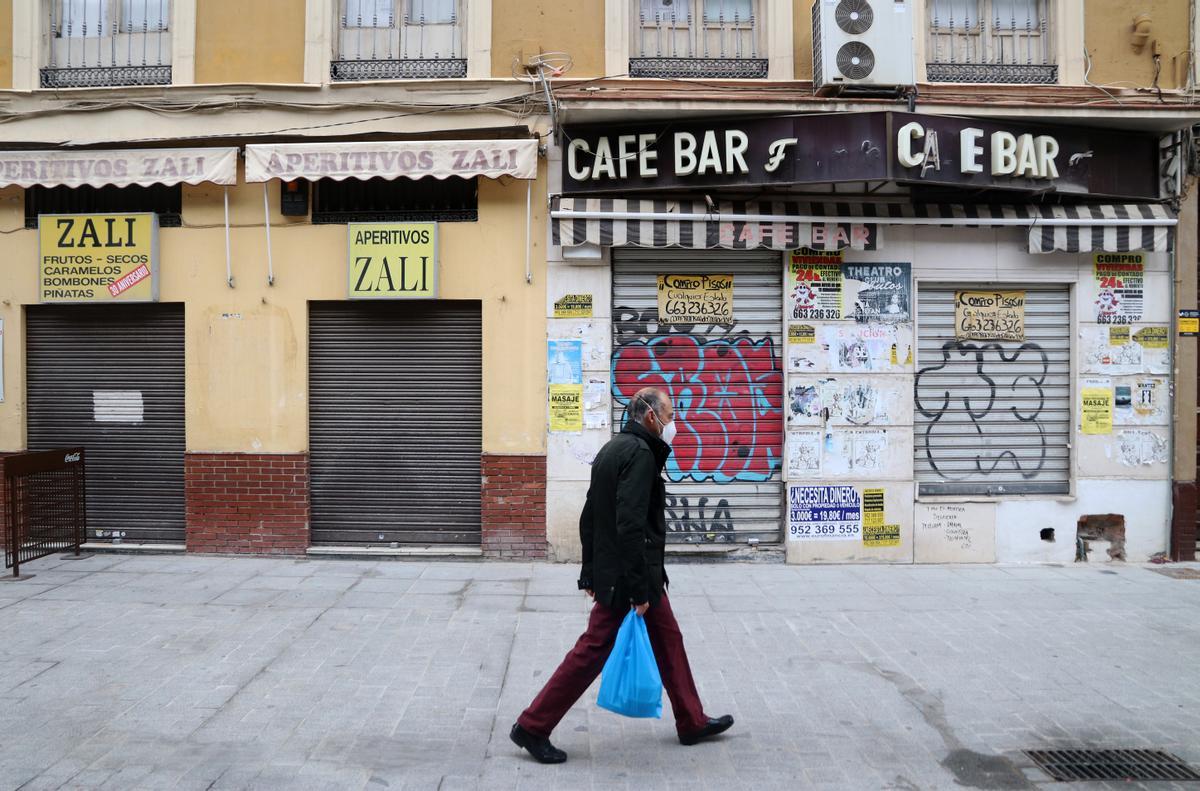 Un hombre camina frente a varios negocios con la persiana bajada en el Centro.