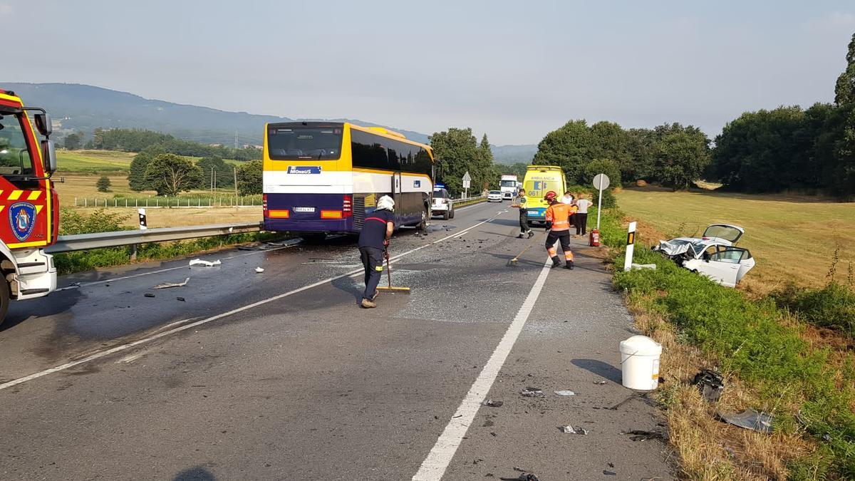 Los bomberos limpian el firme tras el impacto entre el coche y el autobús.// Bombeiros de Deza