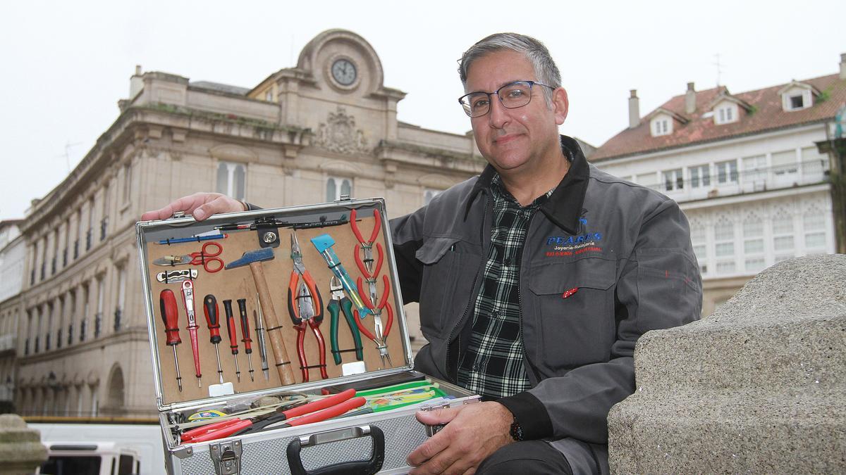 Óscar Pérez, de relojería Peares, con su maletín de trabajo frente a la fachada del Concello en la que se encuentra el reloj.