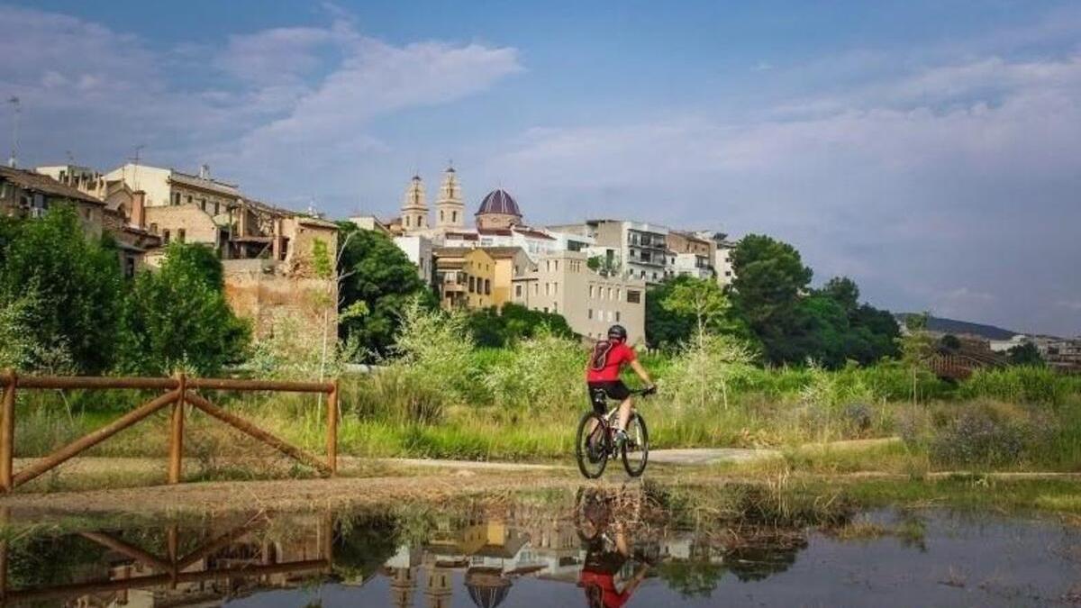 Un ciclista circula por el parque fluvial con Riba-roja al fondo-