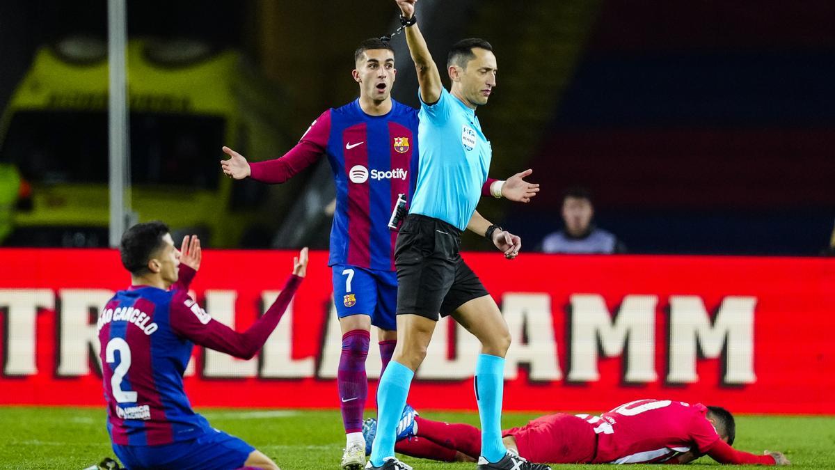 El colegiado Sánchez Martínez saca la cartulina amarilla a Joao Cancelo durante el partido entre Barcelona y Atlético de Madrid.