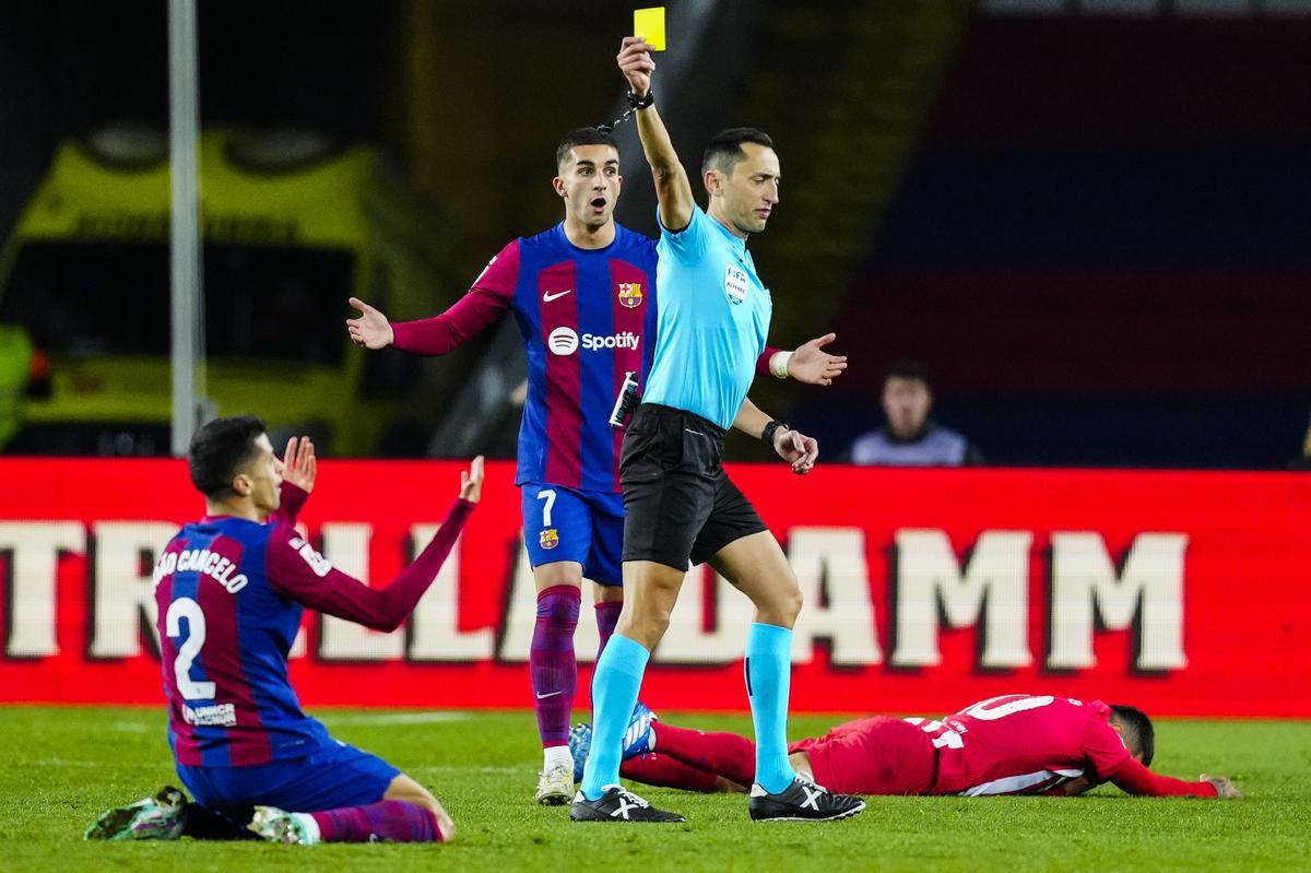 El colegiado Sánchez Martínez saca la cartulina amarilla a Joao Cancelo durante el partido entre Barcelona y Atlético de Madrid.