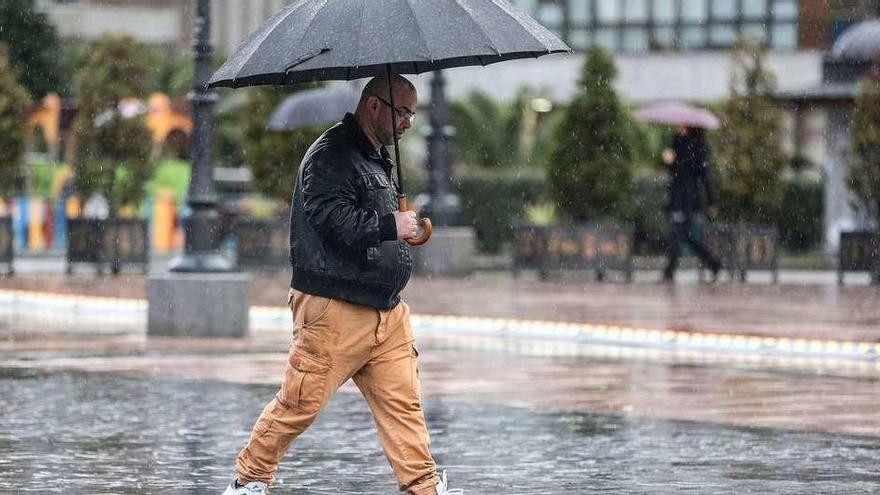 Un hombre, con paraguas, pasea por las calles de Oviedo.