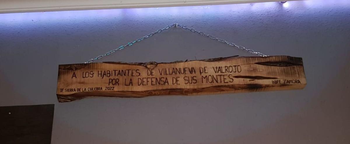 Arriba, el recuerdo sobre el tronco de madera de un árbol quemado que los bomberos forestales han entregado a Villanueva de Valrojo. Abajo, vecinos de Villanueva con bomberos forestales. | A. S.