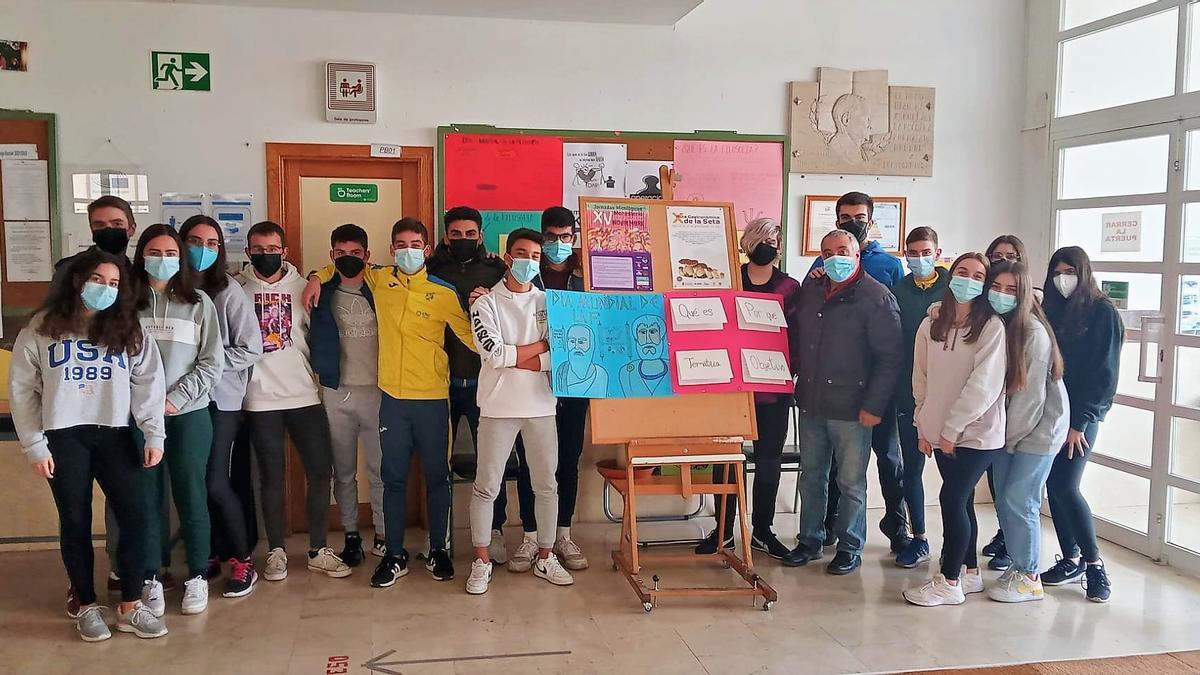 Profesor y alumnado junto a la cartelería que lucen en el hall del centro educativo