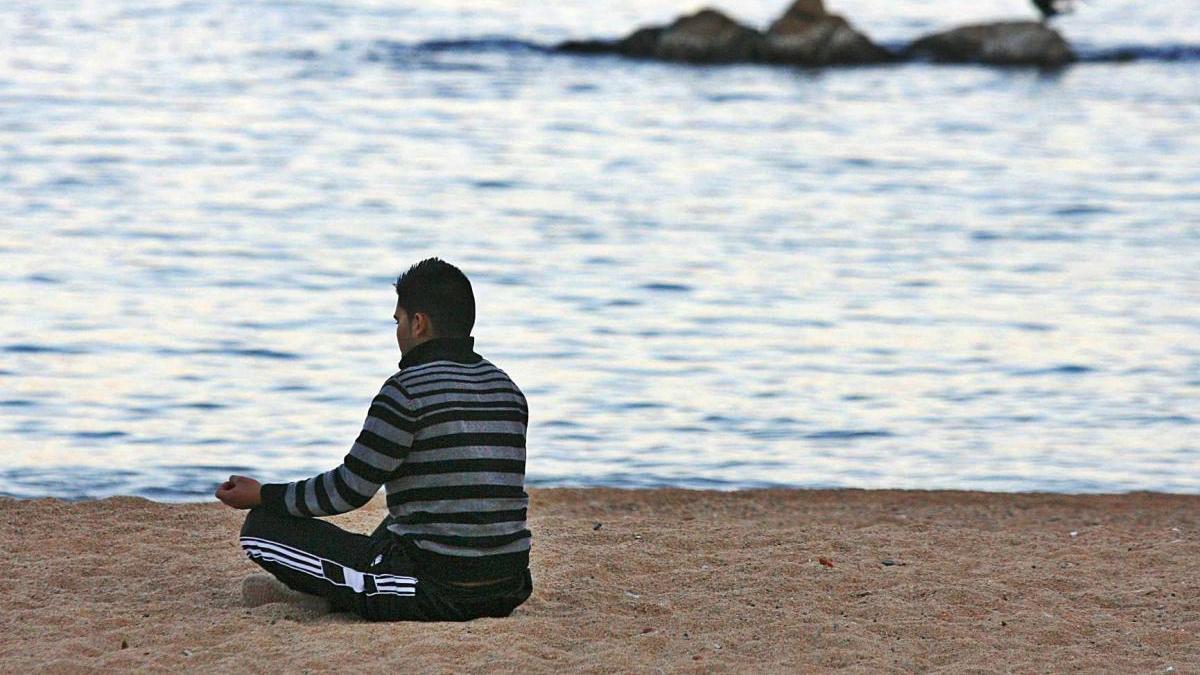 Un home practica la meditació en solitari a la platja.