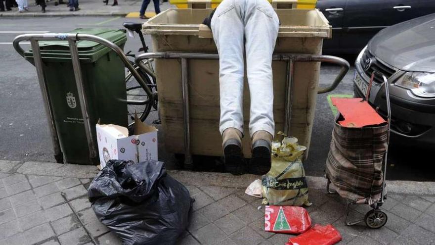 Una persona rebusca en un contenedor de basura en la calle.