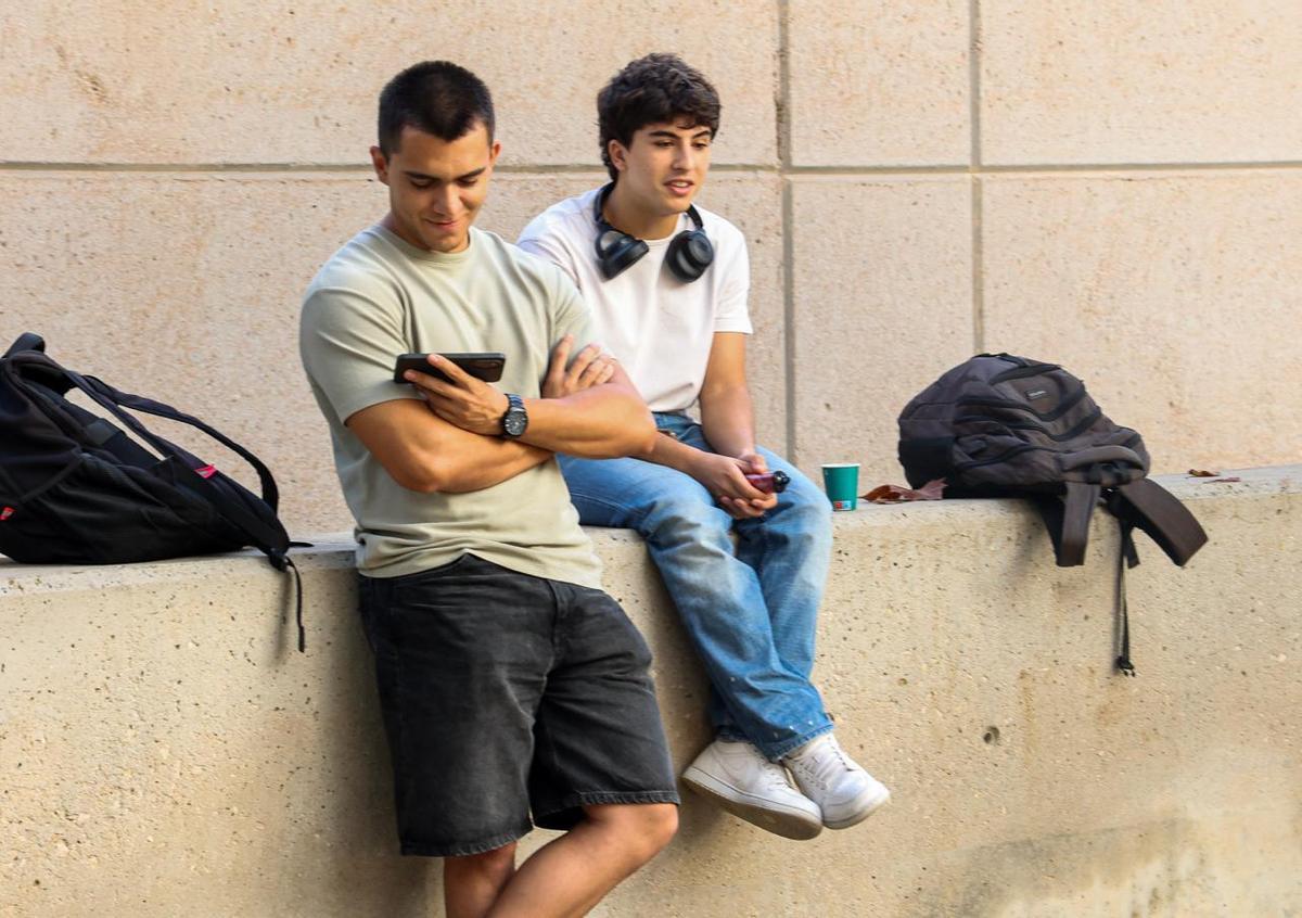 Dos estudiantes charlan y miran el móvil en el descanso de clase
