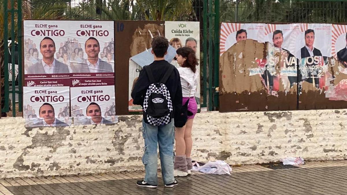 Dos jóvenes, junto a los carteles colocados en la Estación de Autobuses de Elche