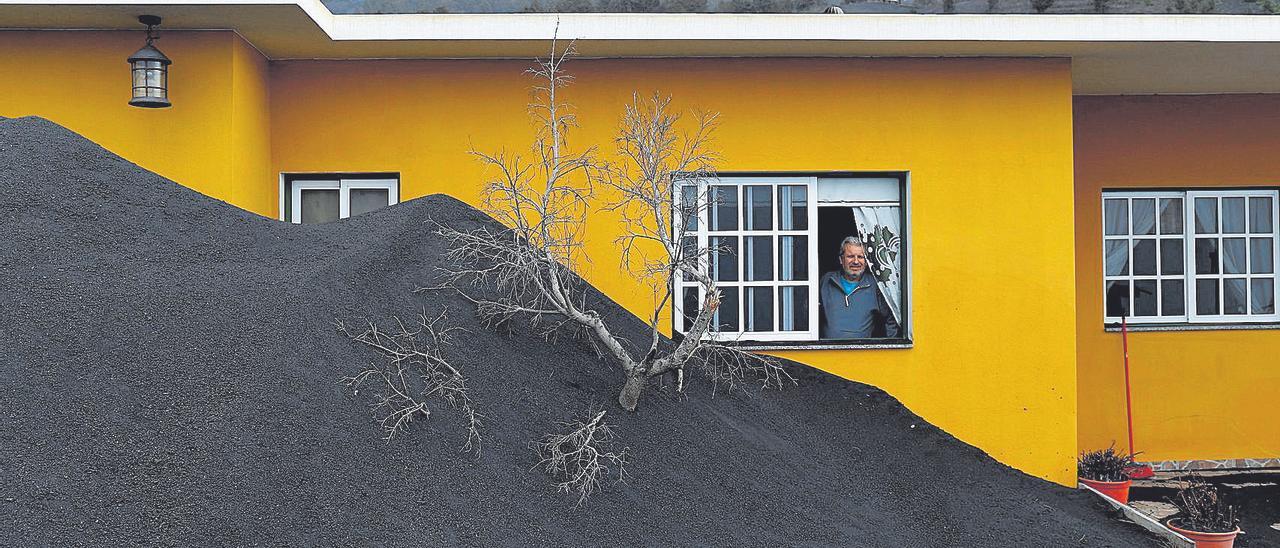 Un vecino de Las Manchas observa a través de una ventana la acumulación de ceniza en un patio.